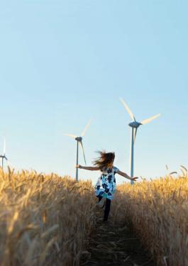Girl running in a field with wind turbines in the background